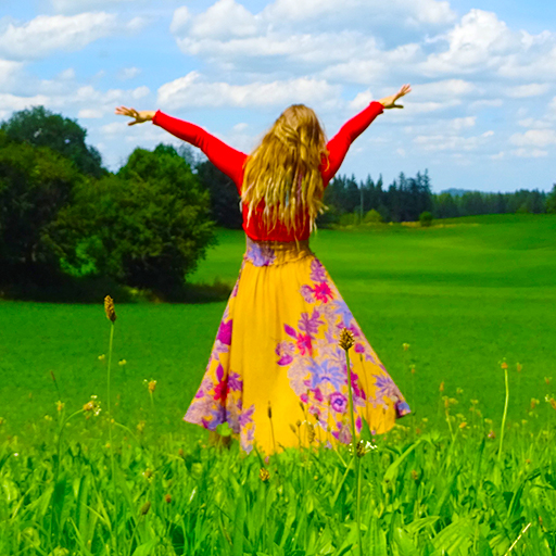 It's a sunny day with blue sky. Juli stand in a Meadow with the back to the camera. In the Background you can see trees. She were a yellow dress with purple, blue, pink flowers on it and a shiny red long arm top. You see her colorful dreads between her normal hair. Both arms up like a dancer.