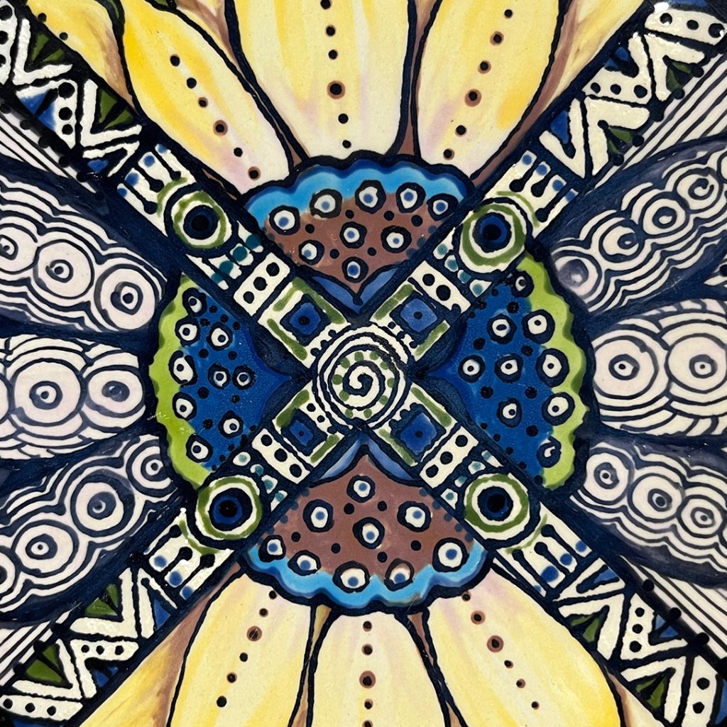 Portfolio Ceramic - Detail view of abstract sunflower plate. A lot mandala geometry in the colors: yellow, light and dark green, light and dark blie, brown, black and white.